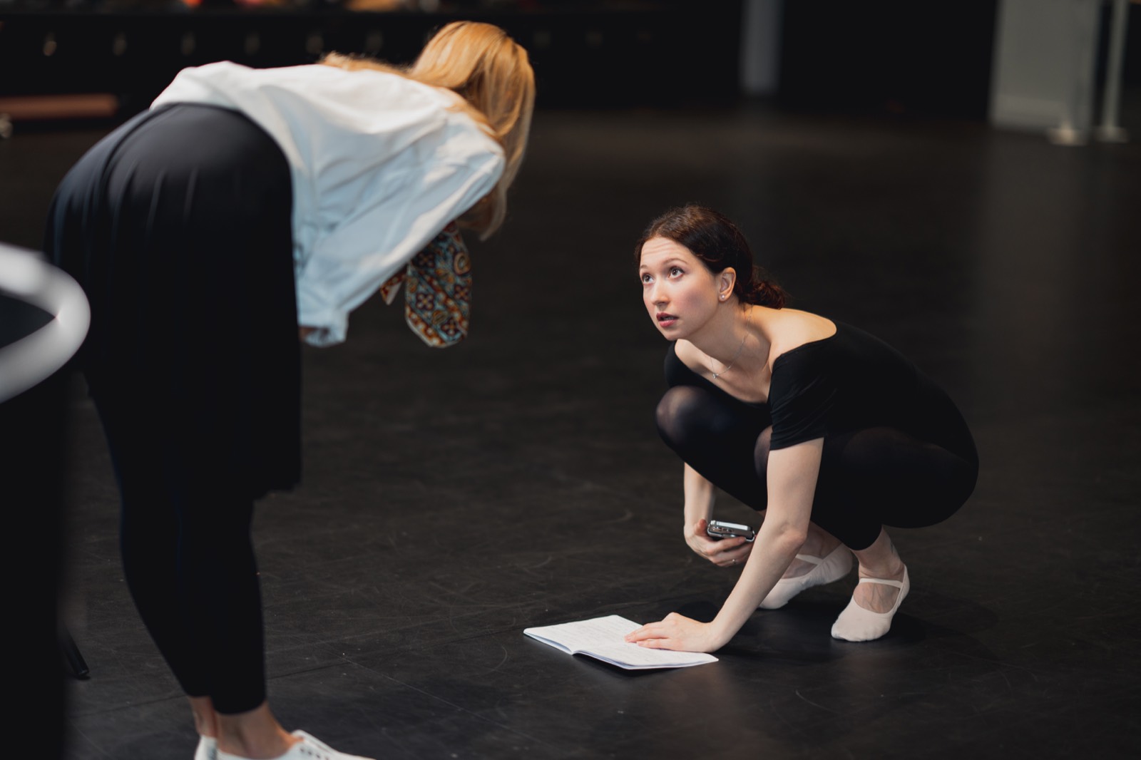 Nina Osman crouching beside a notebook on a studio floor while speaking with a colleague