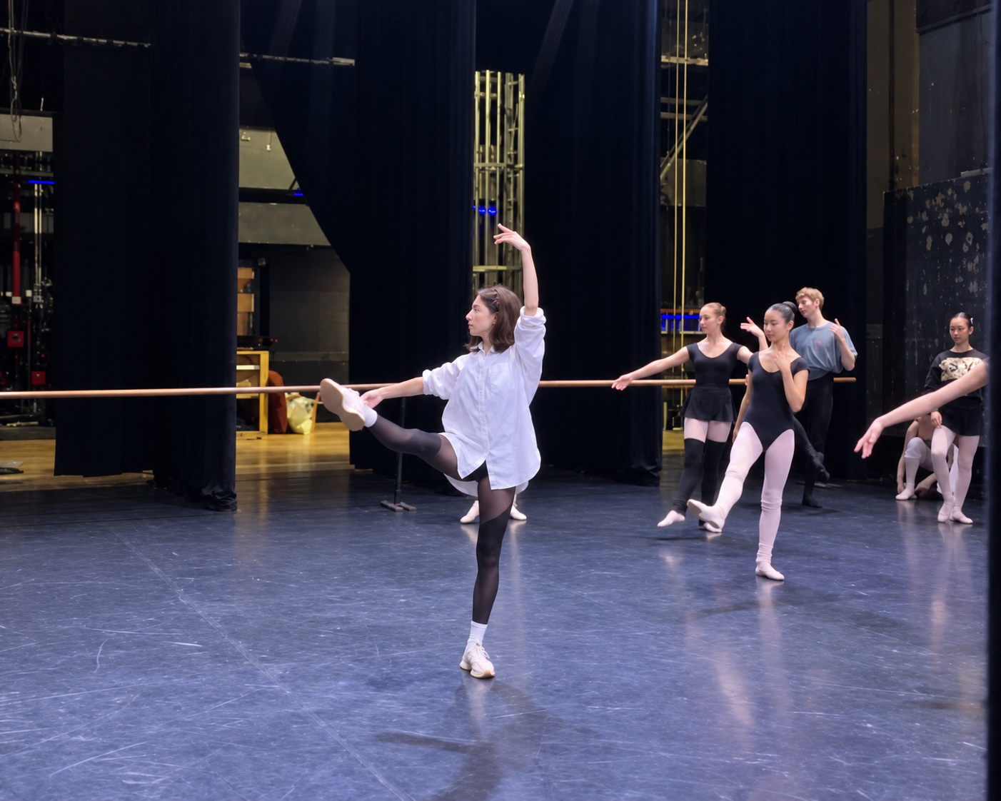 Nina Osman teaching at the barre, one leg lifted, with students behind her